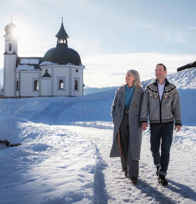 Paar auf Winter-Spaziergang durch Seefeld_Paar läuft vor Seekirchl am späten Nachmittag